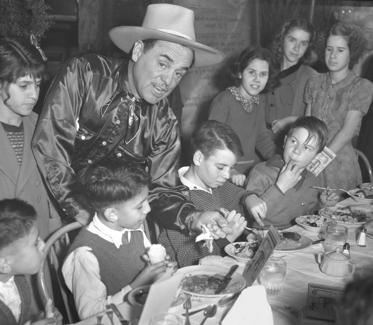 A man in a silk shirt and cowboy hat bands over to take a bite of turkey from a child's plate.