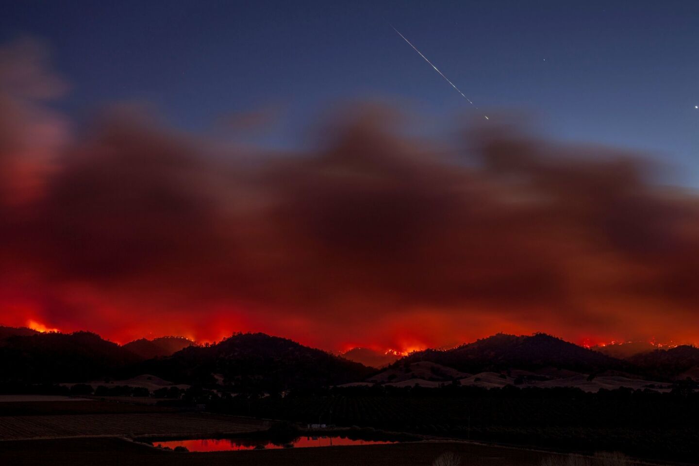 A meteorite falls from the sky, caught in a long time exposure image over the County fire at sunset as it burns out of control in Brooks.
