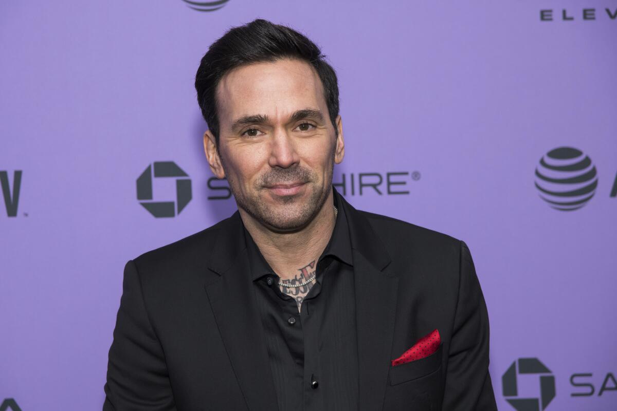Jason David Frank wears a black shirt and blazer in front of a purple background.