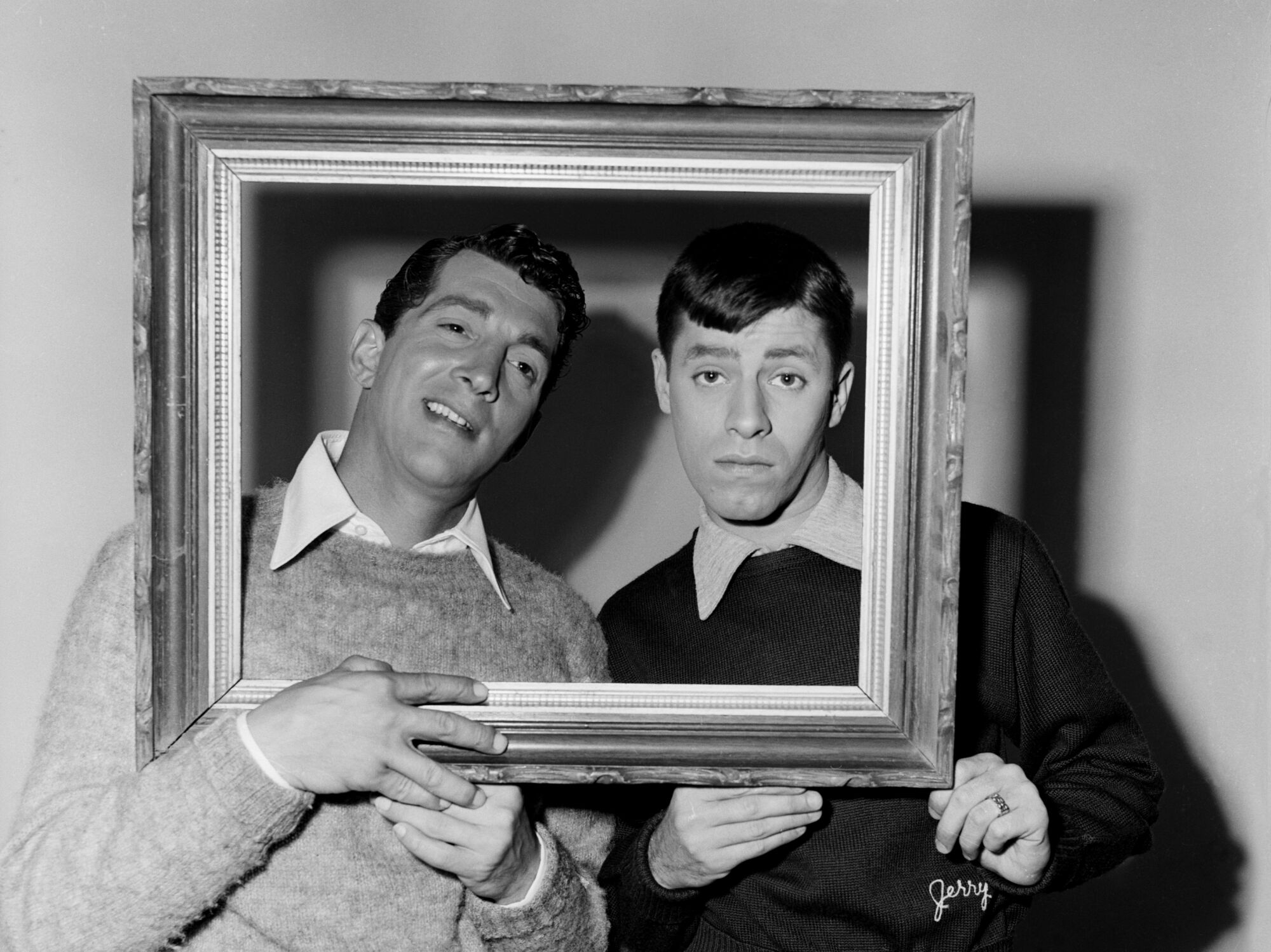 Two men pose for portrait with the heads behind a painting frame.