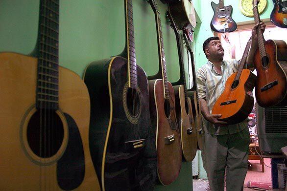 Faiz Khalil shows off some of the guitars in his music shop in Baghdad. He has changed the name of the store to hide the fact that it is run by a Sunni.