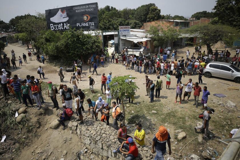 Venezuelan migrants wait in line behind a vehicle for free food being handed out by Colombian residents, as others, below, watch people try to clear a roadblock created by Venezuelan National Guards on the Simon Bolivar International Bridge in La Parada, near Cucuta, Colombia, on the border with Venezuela, Sunday, Feb. 24, 2019. A U.S.-backed drive to deliver foreign aid to Venezuela on Saturday met strong resistance as troops loyal to President Nicolas Maduro blocked the convoys at the border and fired tear gas on protesters. (AP Photo/Fernando Vergara)