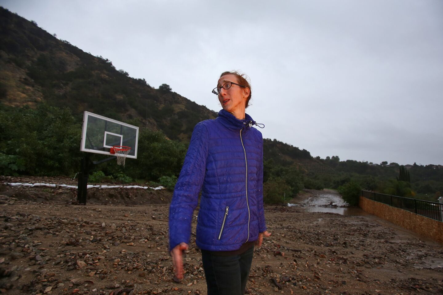 Amanda Heinlein stands by regular size basketball hoop in her backyard at Ridge View Drive that is buried in mud caused by early morning rain in Azusa.