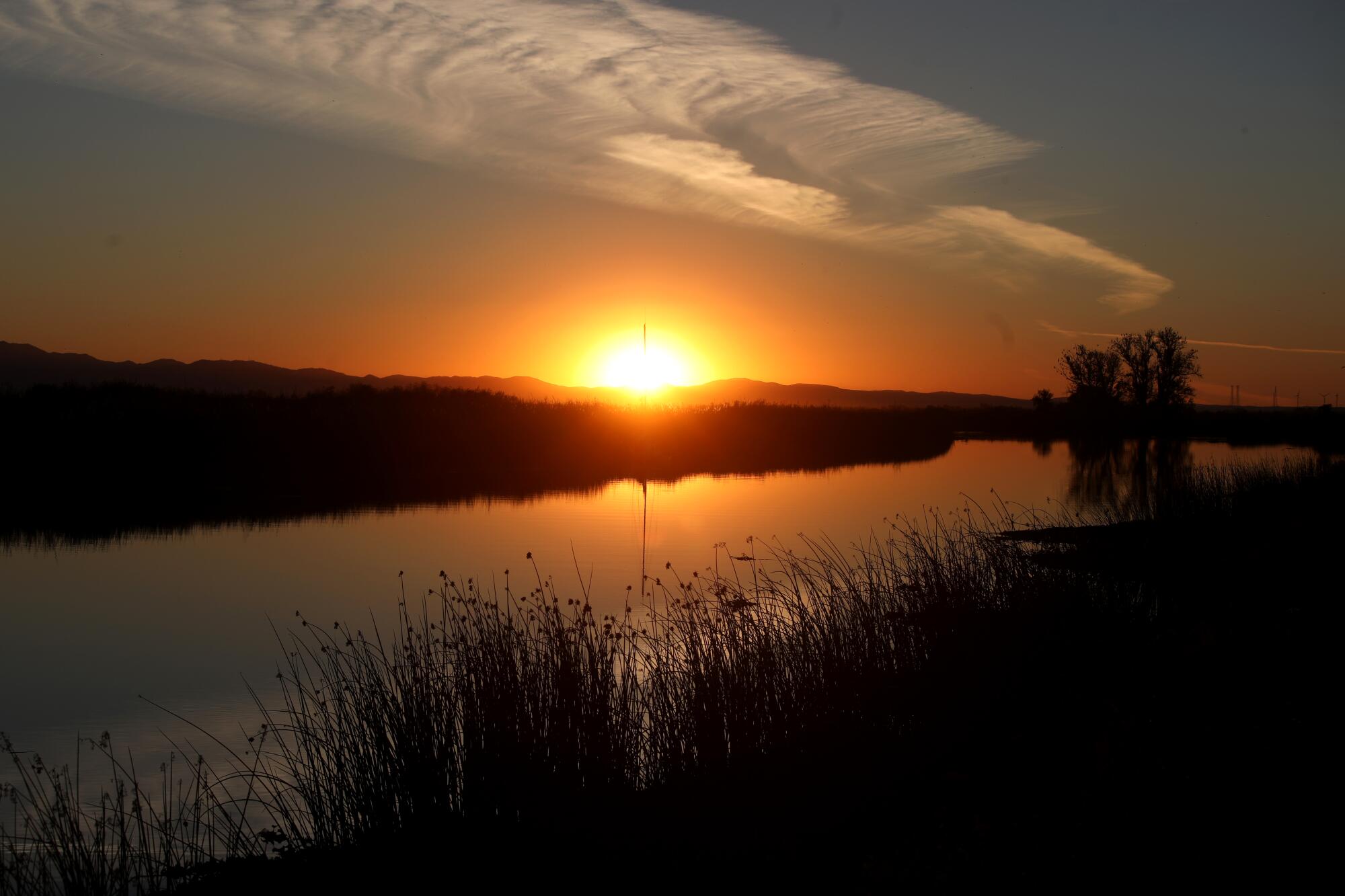 A setting sun gives a river an orange glow.