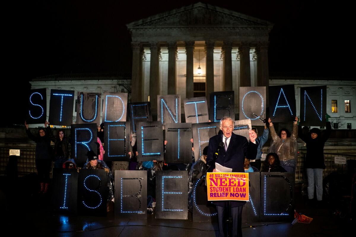 A politician speaks as people around him hold up letters that spell out "student loan relief is legal."