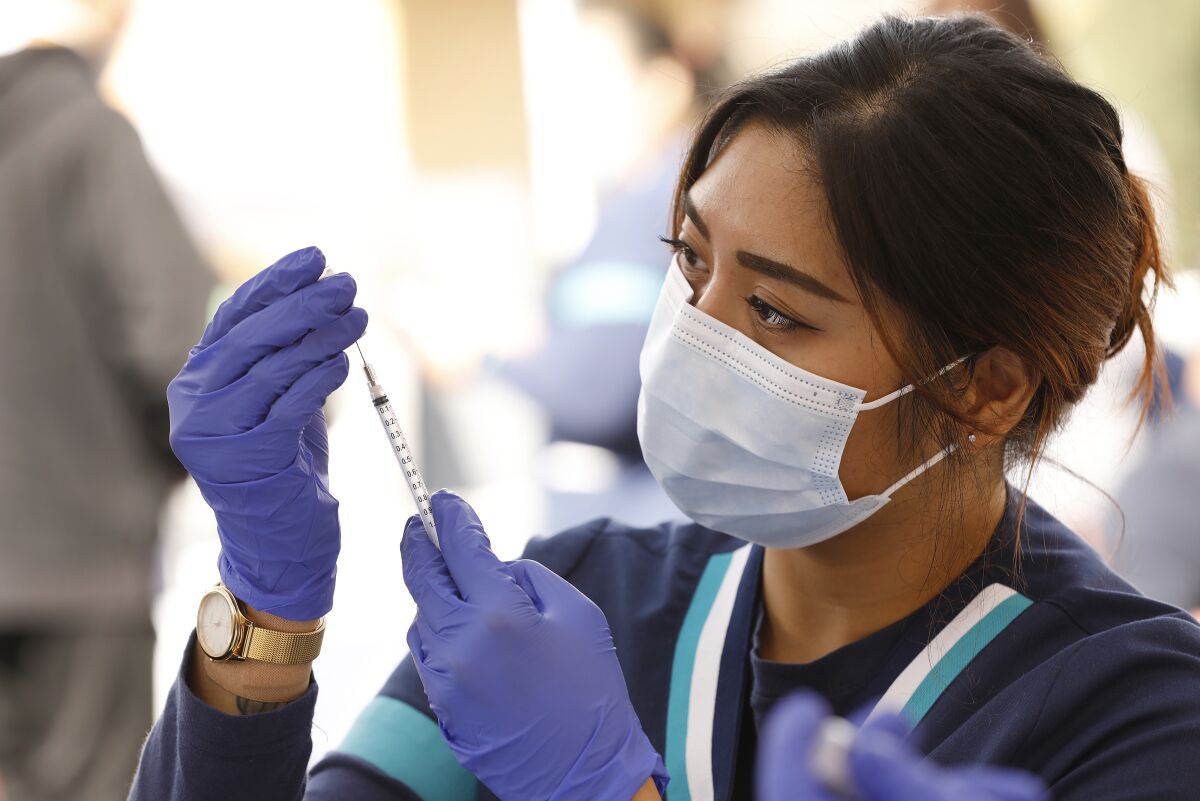 A woman in a mask and gloves looks at a syringe