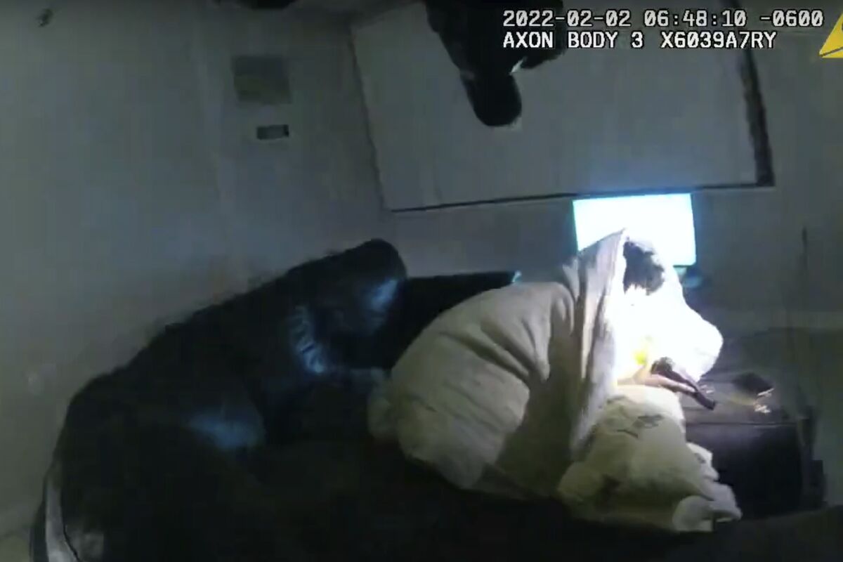 A screenshot from police body camera video shows a man wrapped in a blanket on a couch, holding a gun.