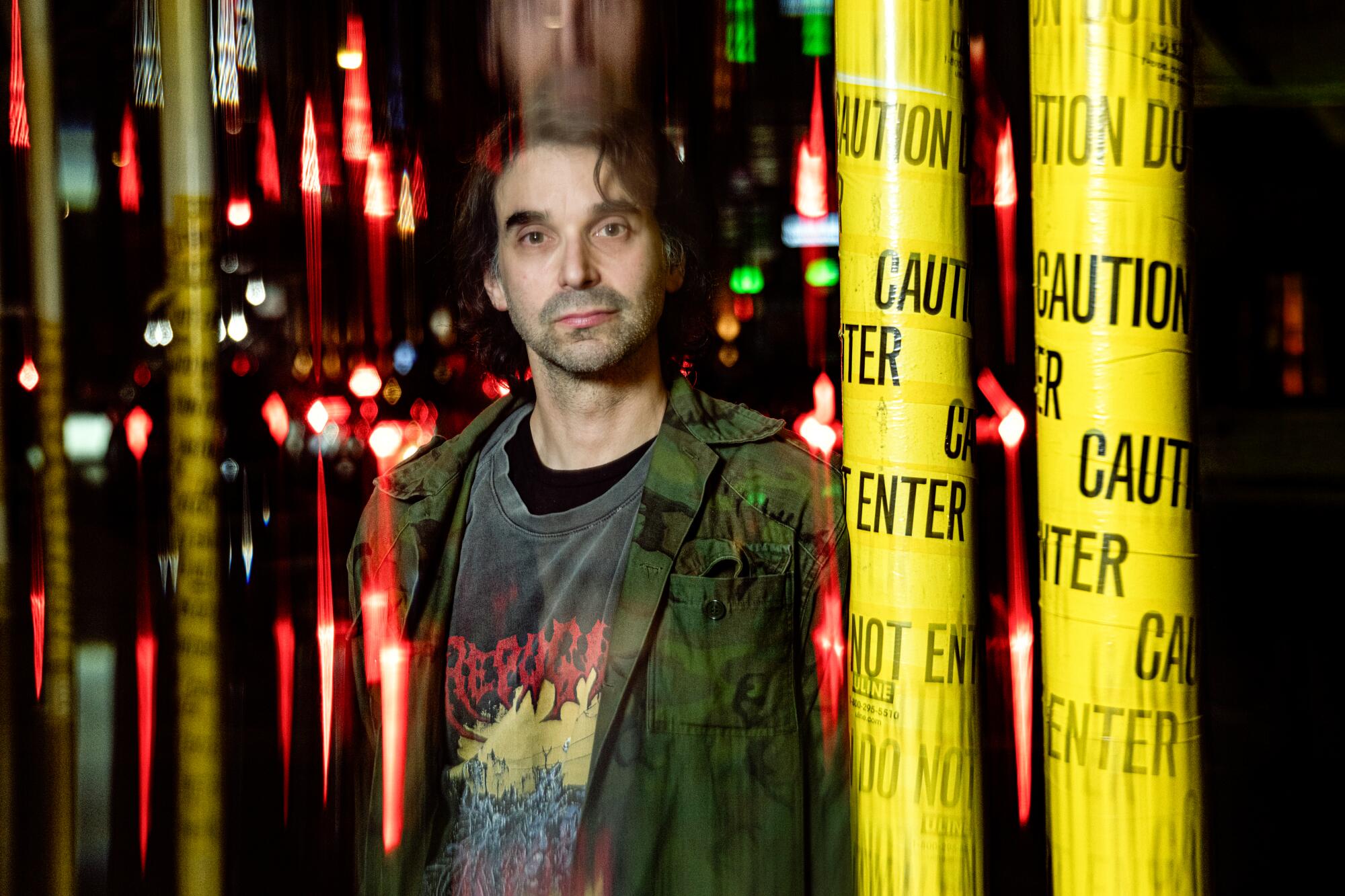 A man in a camo overshirt stands by a yellow-taped construction pole on an urban street.