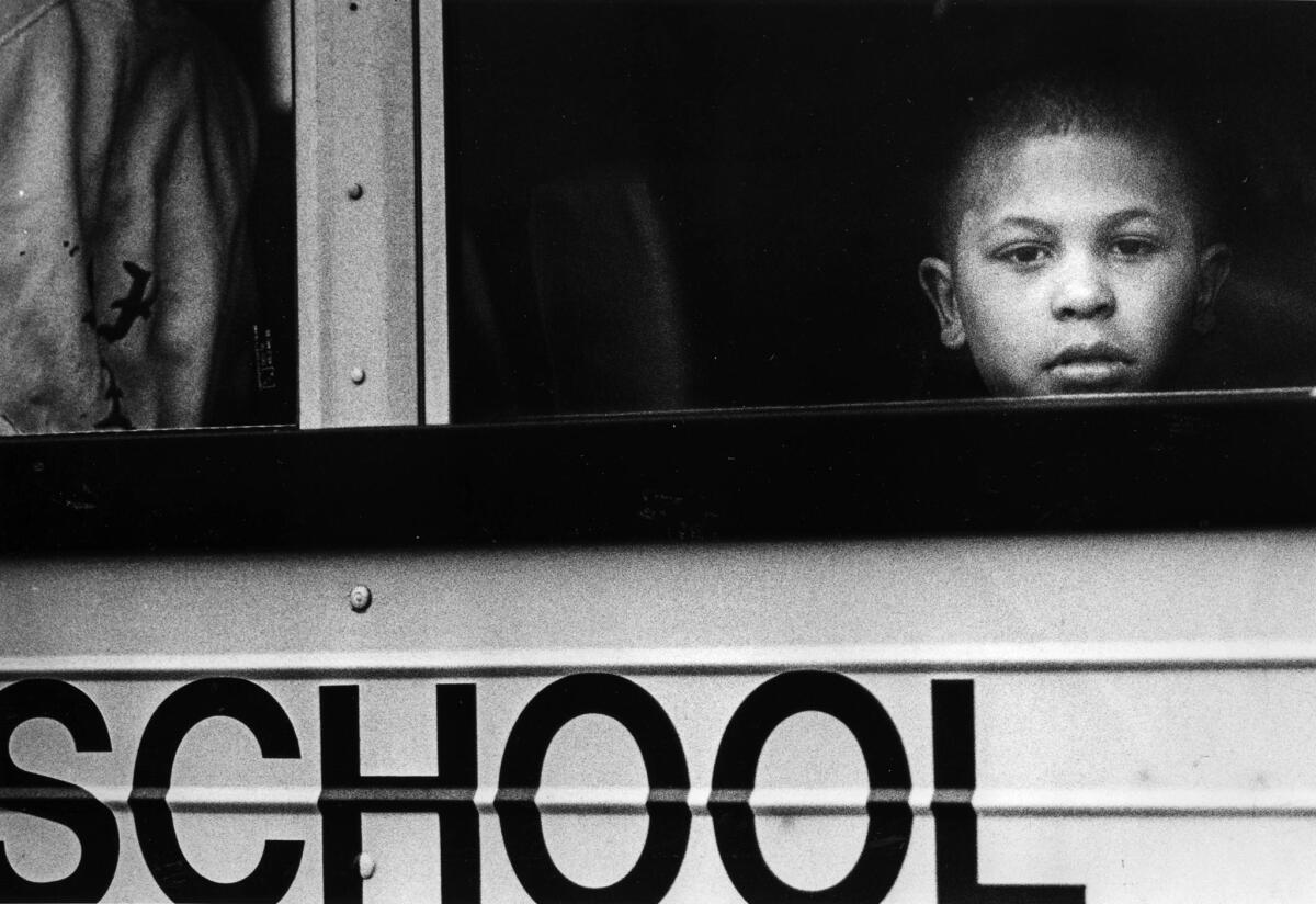 Aug. 14, 1987: A child peers out of a school bus window as she waits for others at the encampment for the ride to Plasencia Elementary School.