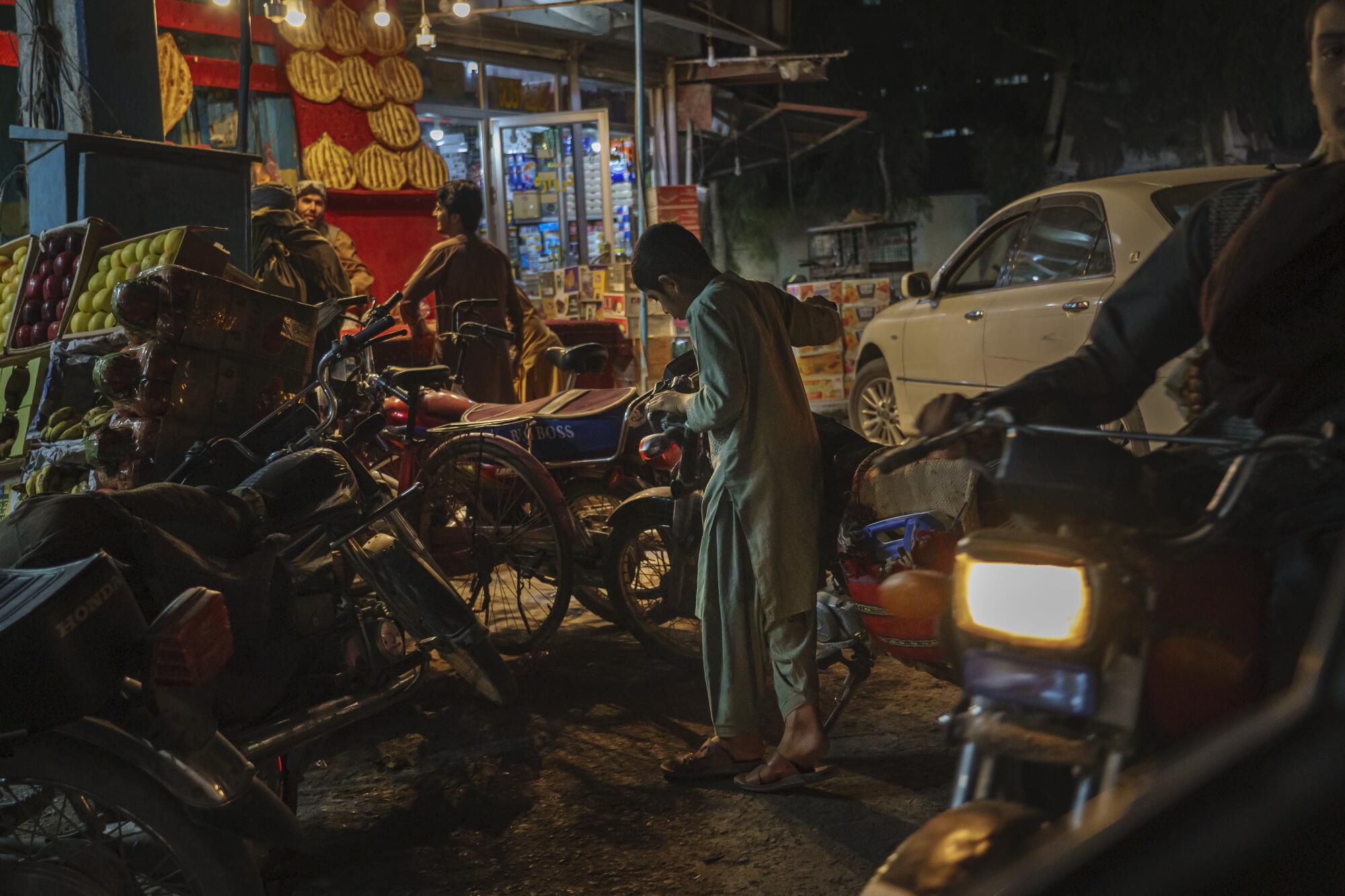 An Afghan boy holds the handlebars of a motorcycle next to boxes of fruit.