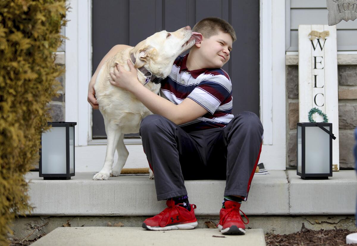 Nolan Balcitis, 12, sits in front of his family's home in Crown Point, Ind., hugging his dog Callie 