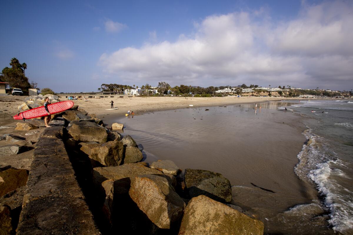 A surfer stands on the breakwater at Doheny State Beach. 