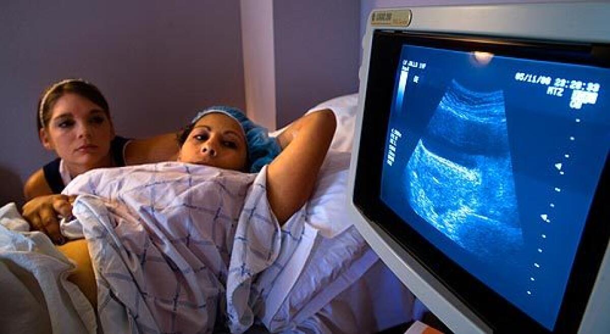 Angel Howard and her friend Liz Rosario watch an ultrasound screen as a doctor transfers two embryos into her uterus. Howard, a military wife and mother of six, is acting as a surrogate for a French couple. Audio slide show >>>>