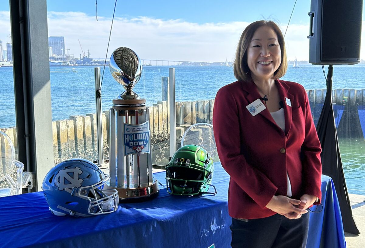 Cherry Park, 2022 Holiday Bowl president, stands with the game trophy and helmets of this year's participating teams.