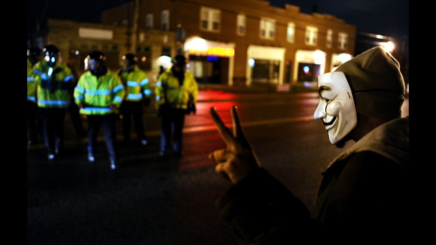 A protester flashes a peace sign as police officers approach along South Florissant Road in Ferguson, Mo., on Nov. 22.