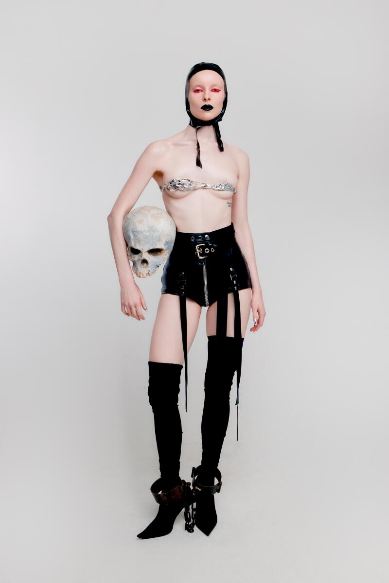 A woman wearing black leather holds a skull.