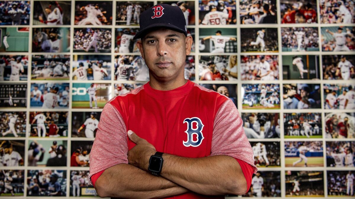 Alex Cora poses in front of a wall of photographs depicting every win throughout the season.