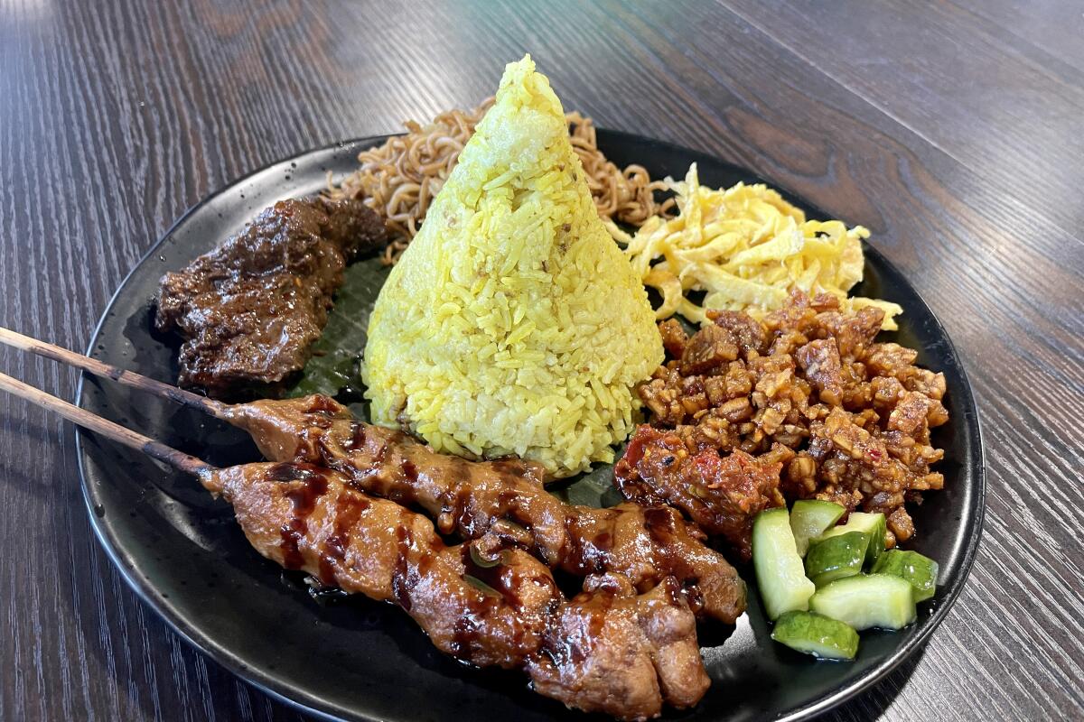 Meat on skewers, cucumber chunks, a pyramid of rice and other dishes on a round plate