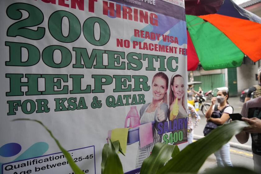 A woman stands beside a sign about hiring domestic helpers for the Mideast outside an office in Manila, Philippines on Thursday, Oct. 21, 2021. The Philippines, a leading source of global labor, has fought with alarm the spike in the number of Facebook pages, which have been used for illegal job recruitment and human trafficking in the last two years. Facebook suggested a pilot program to begin in 2021 that targeted Filipinas with pop-up messages and banner ads warning them about the dangers working overseas can pose. (AP Photo/Aaron Favila)