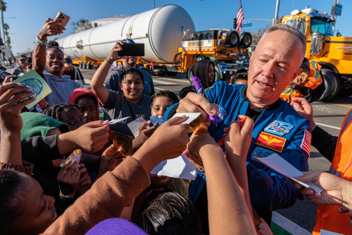 A man in a flight suit signs autographs for children.