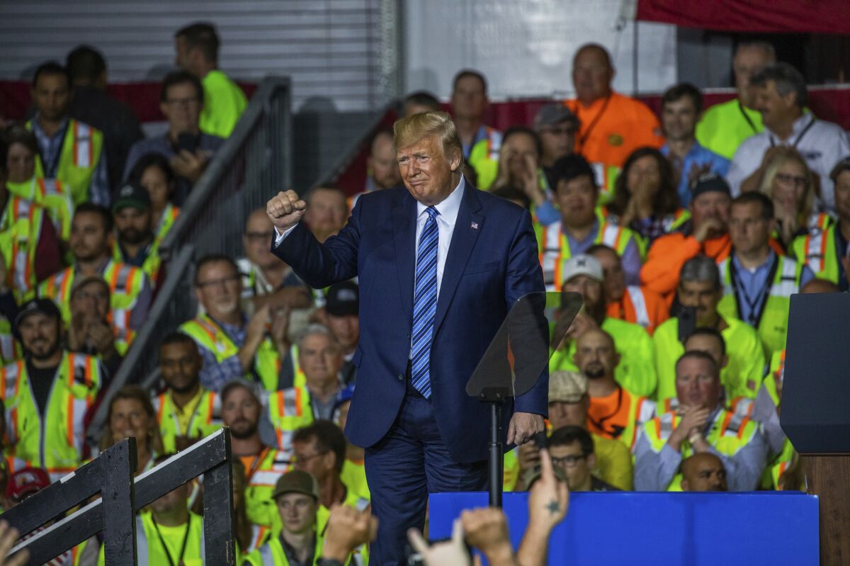 Workers at a Pennsylvania petrochemical plant in yellow vests listen to Trump, who raises a clenched fist.