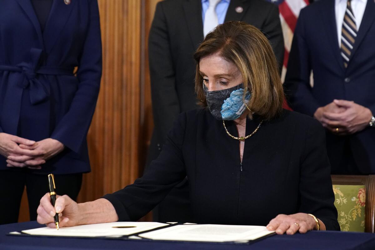 Nancy Pelosi, seated with pen in hand, signs a document.
