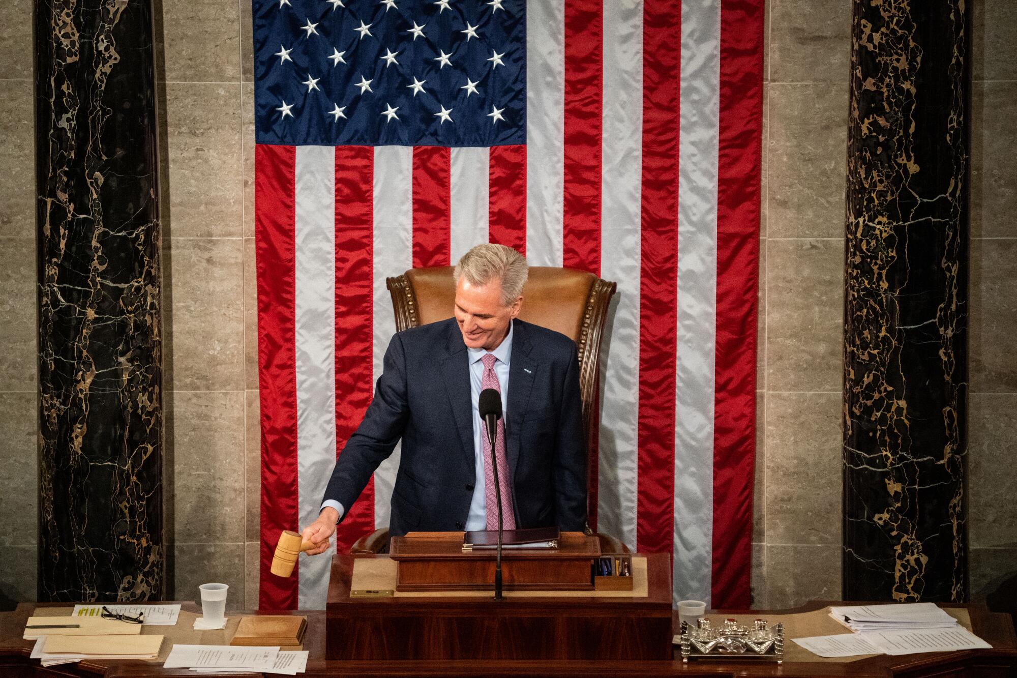 A man in a suit bangs a gavel while standing at a lectern in front of the U.S. flag.