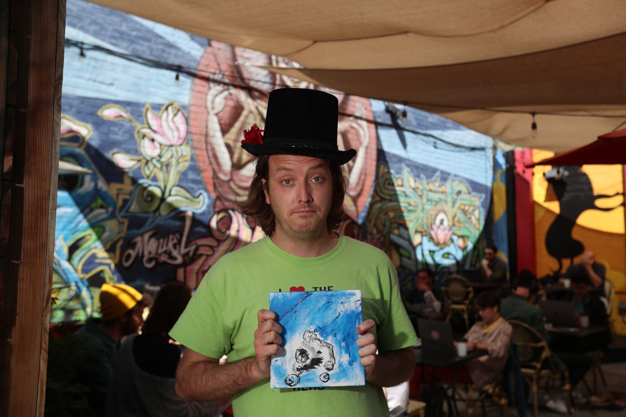 A man in a top hat and a neon green T-shirt holds a painting.
