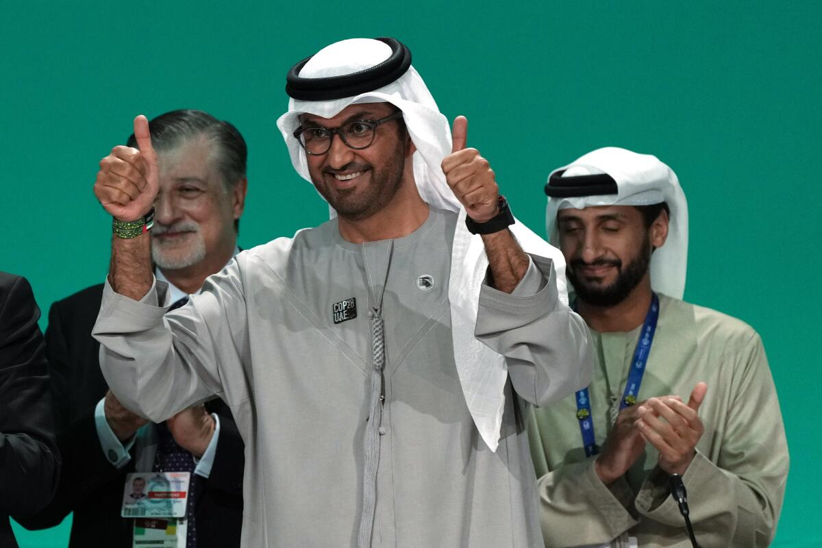COP28 President Sultan Al Jaber gives two thumbs up while two men behind him clap.