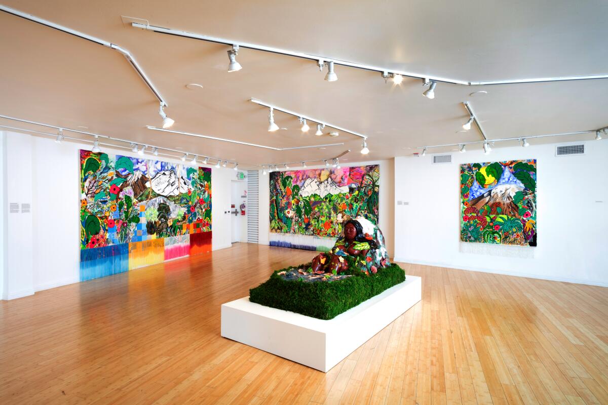 A gallery space with paintings on the wall and a sculpture of a woman sitting in grass at the center.