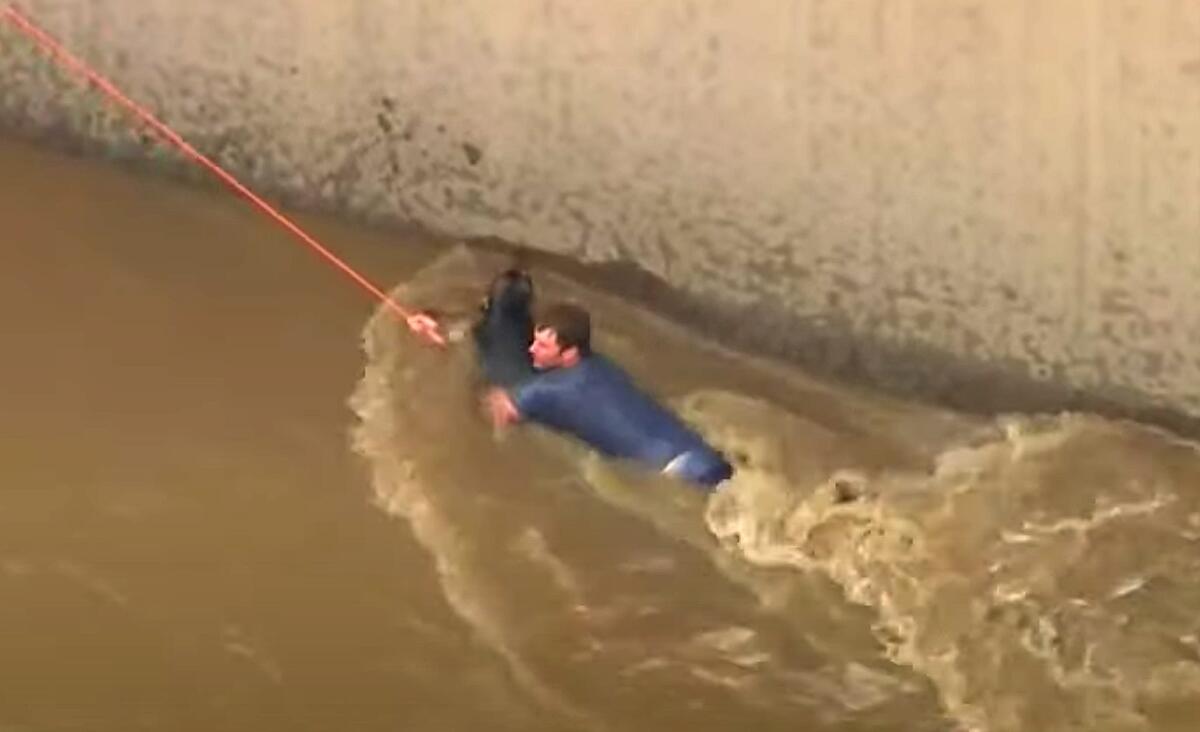 A man grabs onto a dog and is pulled by a rope in the L.A. River