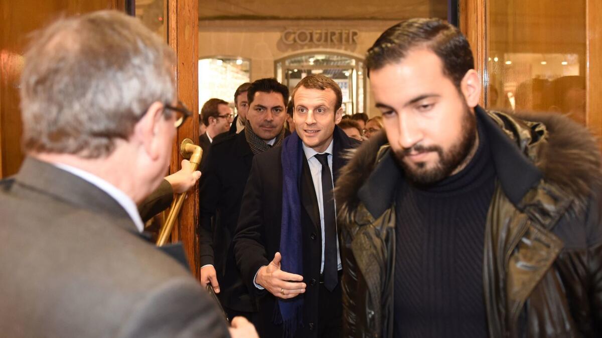 In this Dec. 13, 2016 photo, French President Emmanuel Macron, center, is escorted by his bodyguard, Alexandre Benalla, right, into a library before a book-signing.