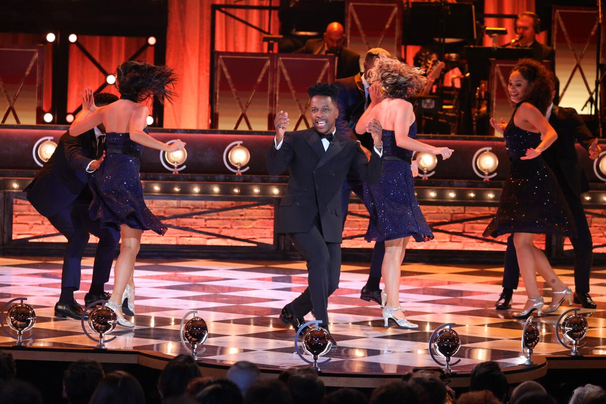 Leslie Odom Jr., in a black tux, performs before a row of dancers on a stage.