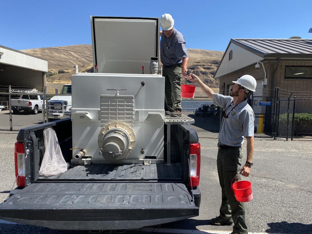 Men in hard hats hold buckets next to a pickup truck with a tank in the bed. 