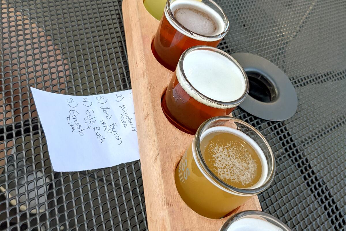 Flight of five beers, sitting in a wooden serving board on a wire mesh table