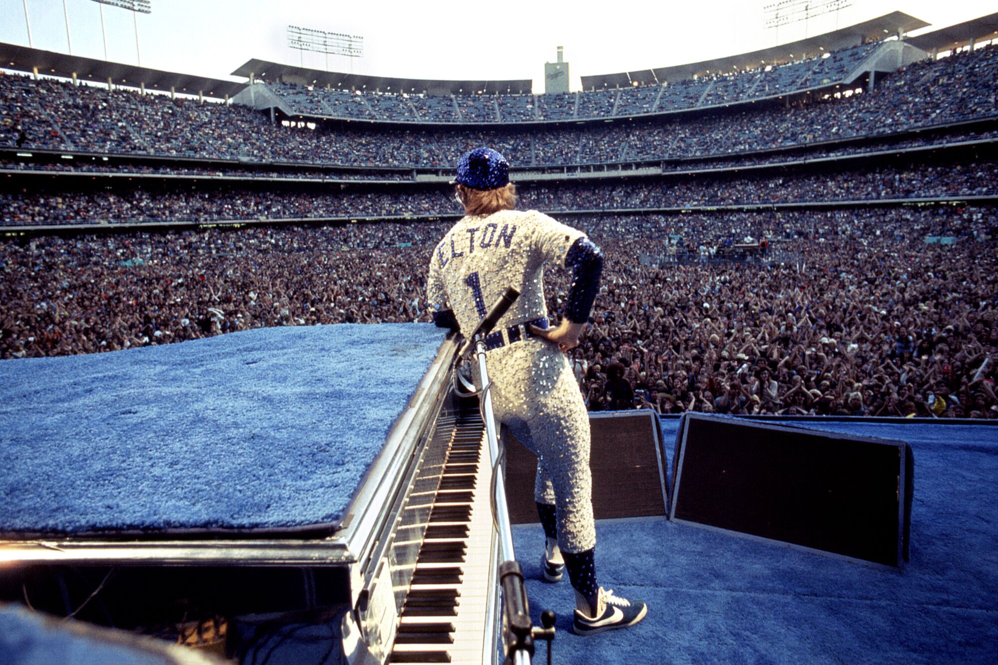 A musician onstage in a sequined Dodgers uniform looks out over a stadium full of fans