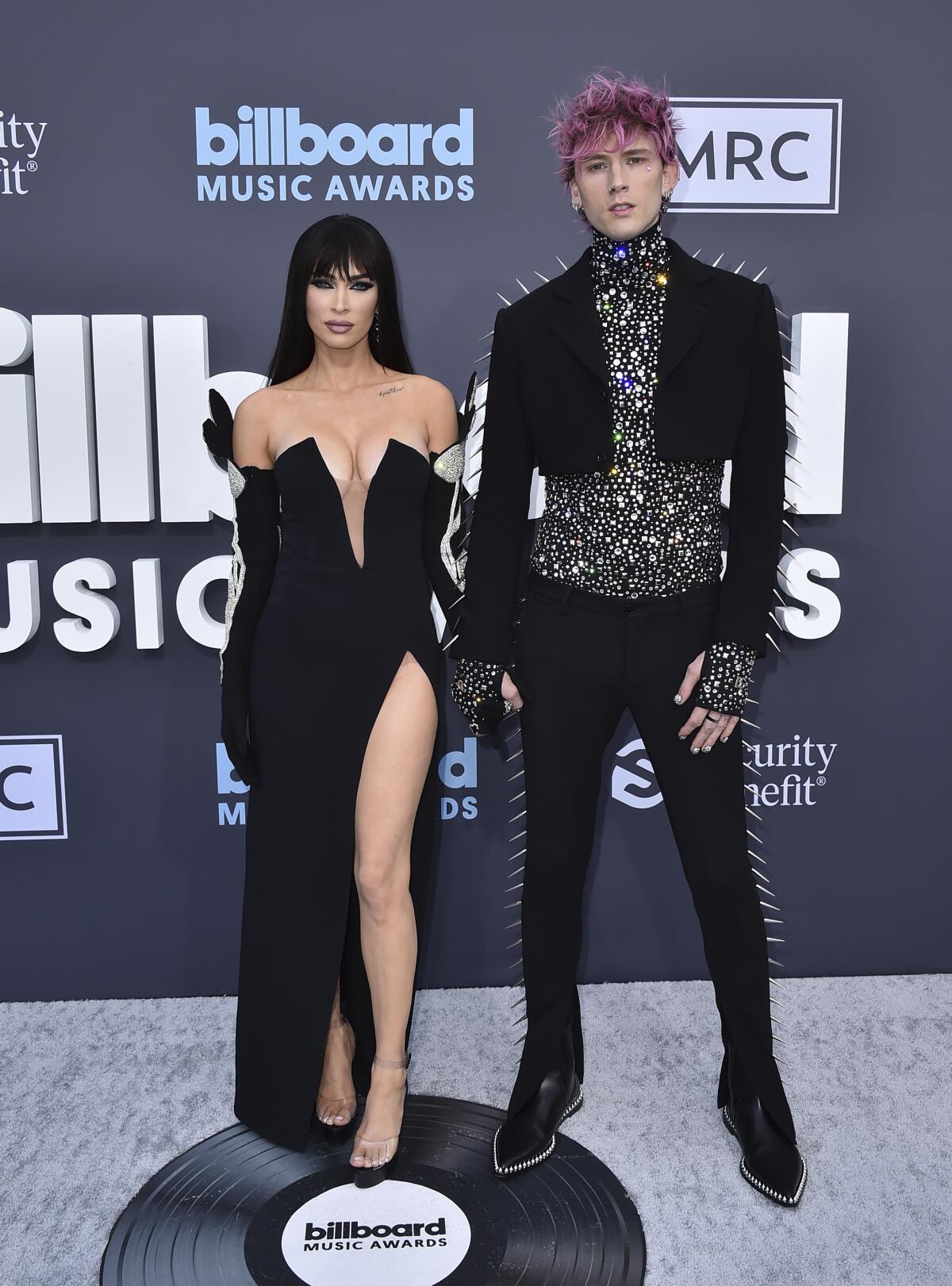 Megan Fox in a black gown and musician Machine Gun Kelly in a spikey black suit pose for cameras on a gray carpet