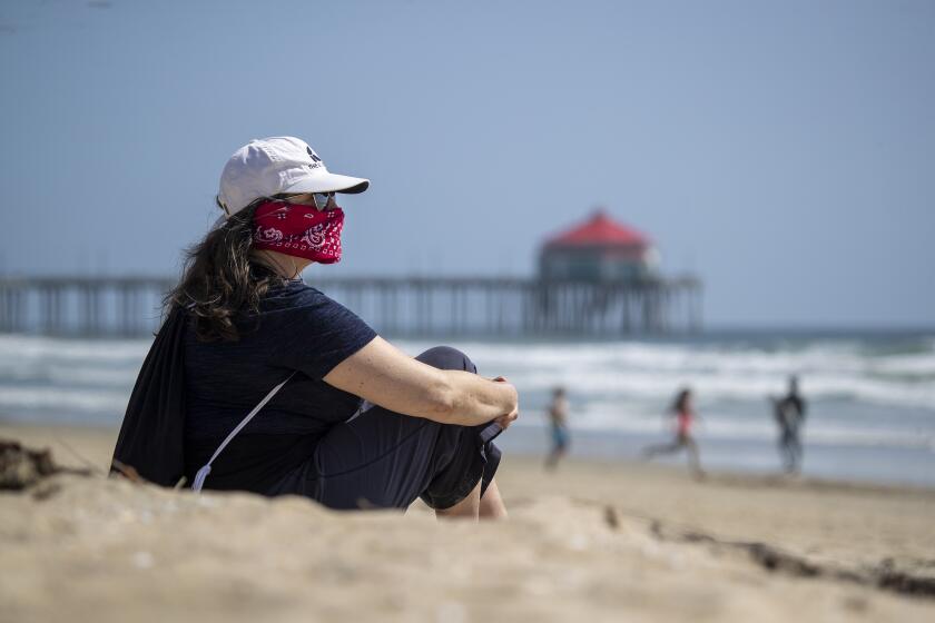 HUNTINGTON BEACH, CALIF. -- THURSDAY, APRIL 2, 2020: Kelly Beita, of Huntington Beach, wears a bandana to help protect her and others from possible Coronavirus exposure, takes a break from working from home, to relax and walk on the beach in Huntington Beach Thursday, April 2, 2020. Beita said she read that it's possible Coronavirus is in the water and the air at the beach and that her friend is making one for her. (Allen J. Schaben / Los Angeles Times)