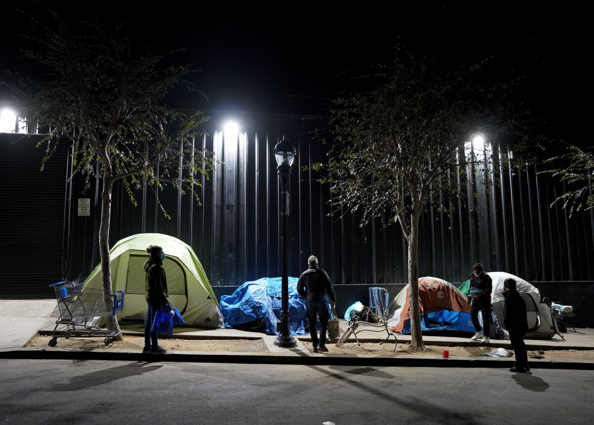 People stand alongside small tents on a city sidewalk.