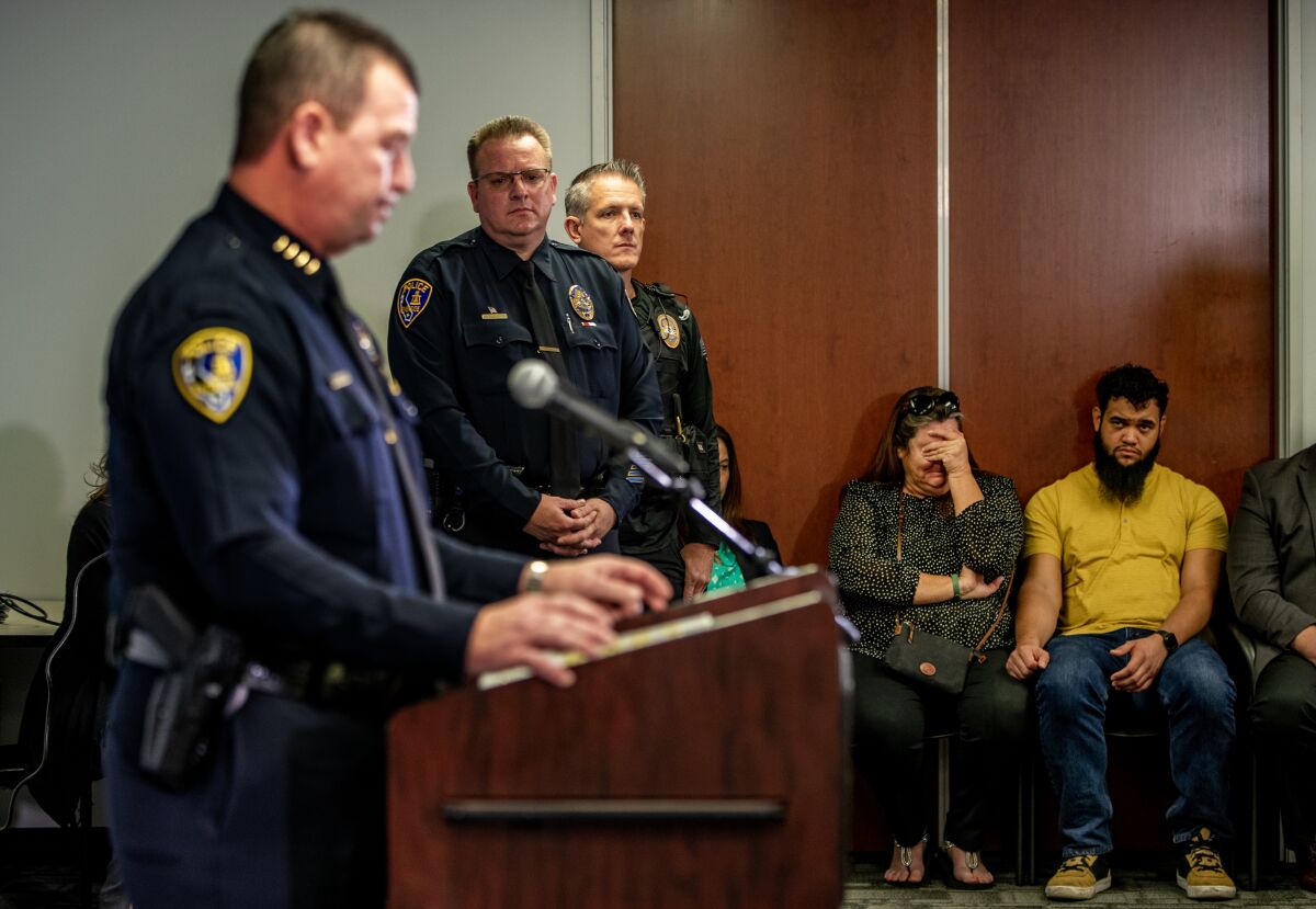 A family member covers her face as Riverside Police Chief Larry Gonzalez discusses the killings.
