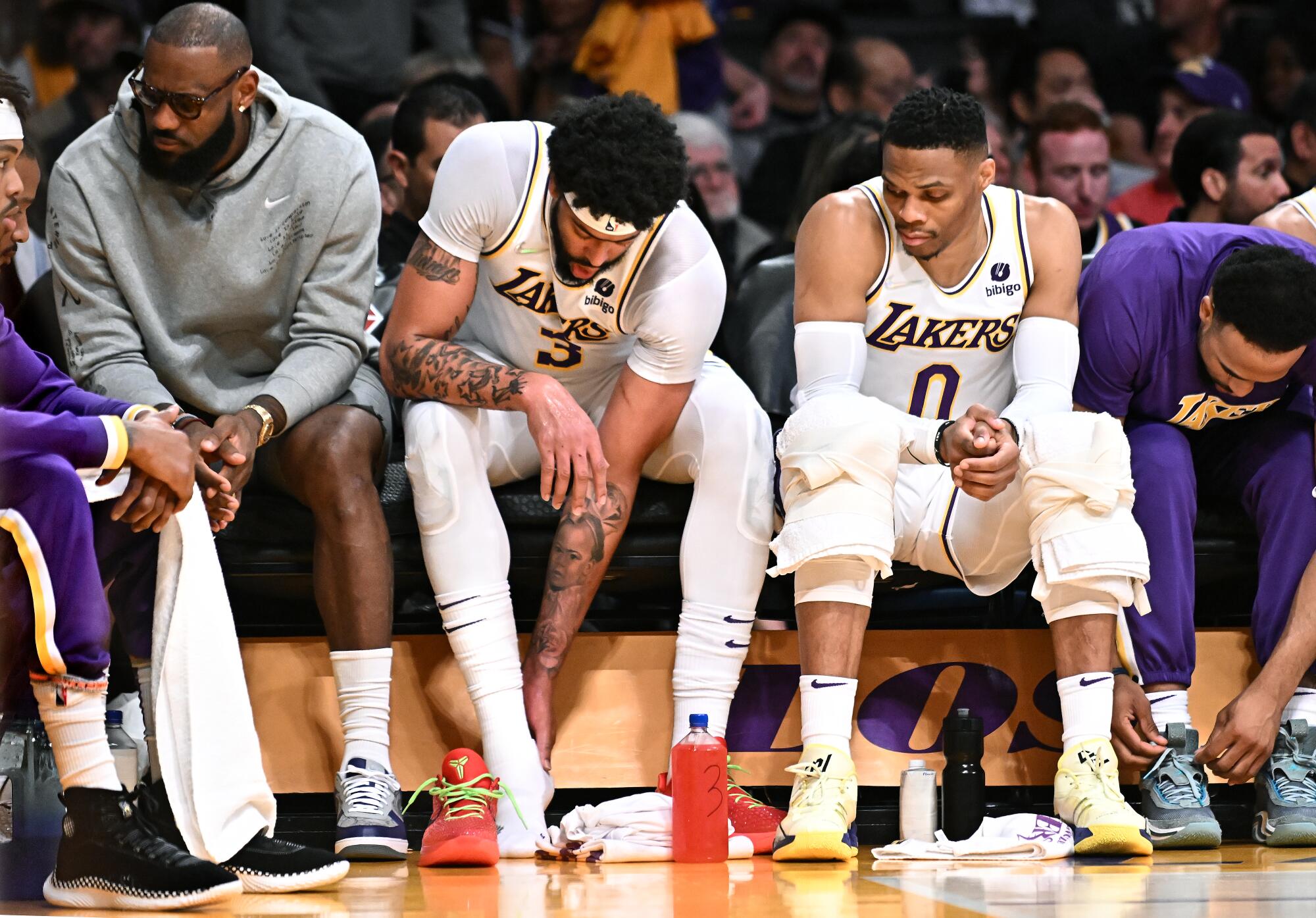 Lakers star Anthony Davis holds his ankle as a sidelined LeBron James and Russell Westbrook sit next to him.