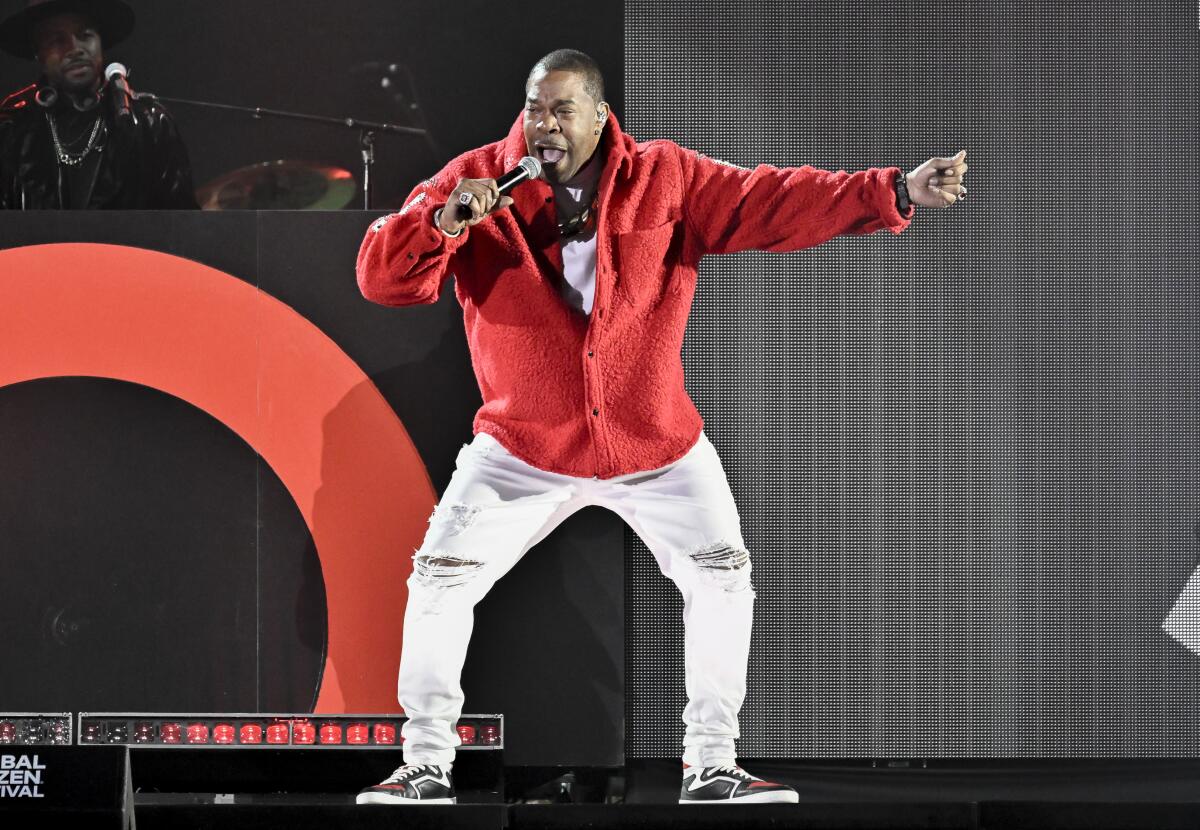 Busta Rhymes wears a red jacket and white pants while performing onstage
