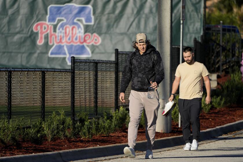 El primera base de los Filis de Filadelfia Alec Bohm, izquierda, llega para los trabajos de campo de primavera el miércoles 14 de febrero de 2024, en Clearwater, Florida. (AP Foto/Charlie Neibergall)