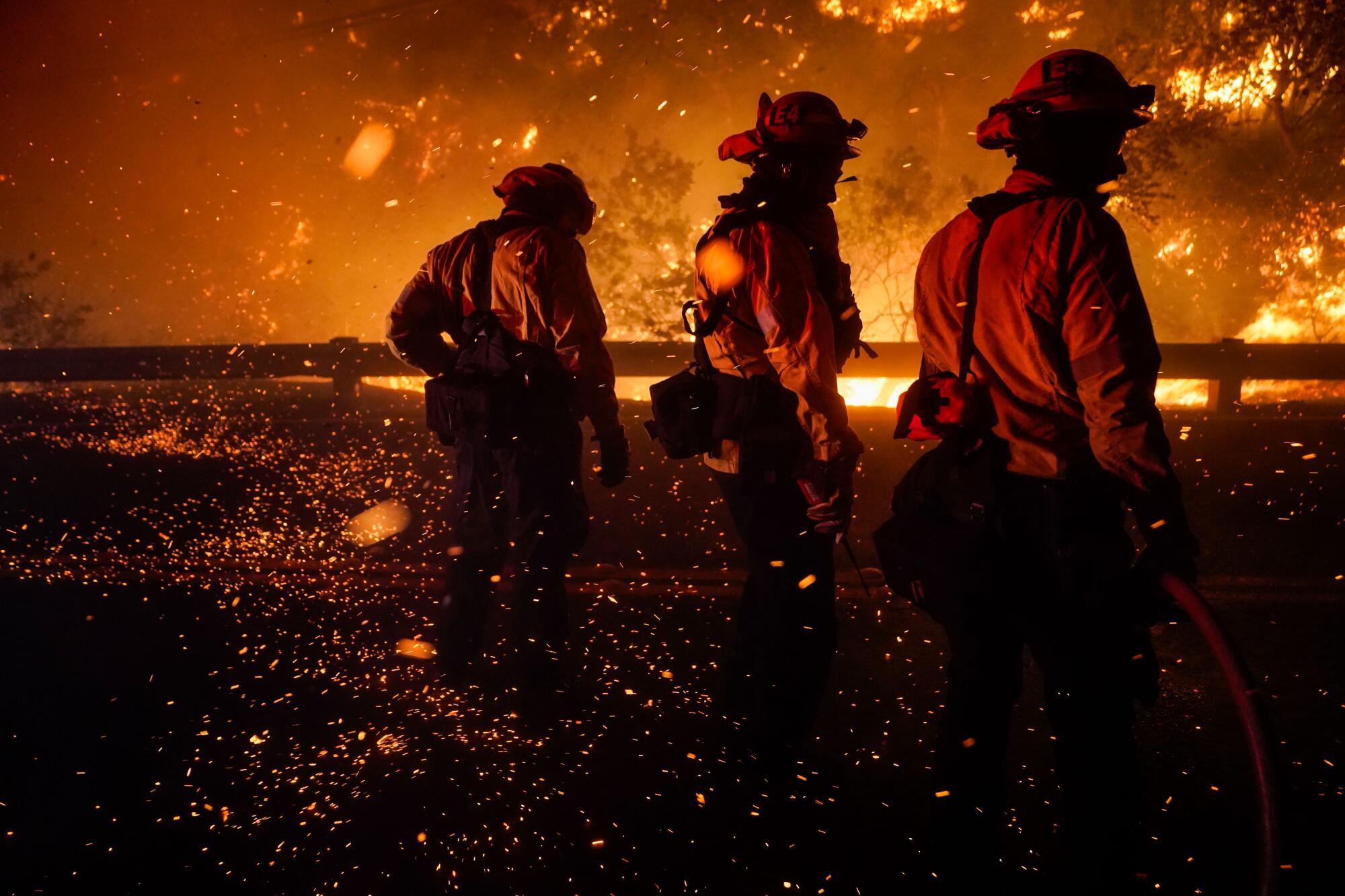 Firefighters silhouetted by orange flames at night with embers floating