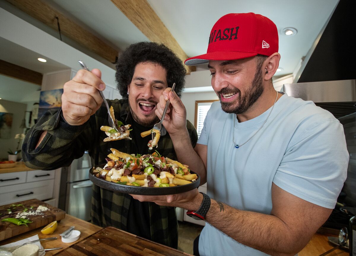 Two men pick at a plate of food with forks