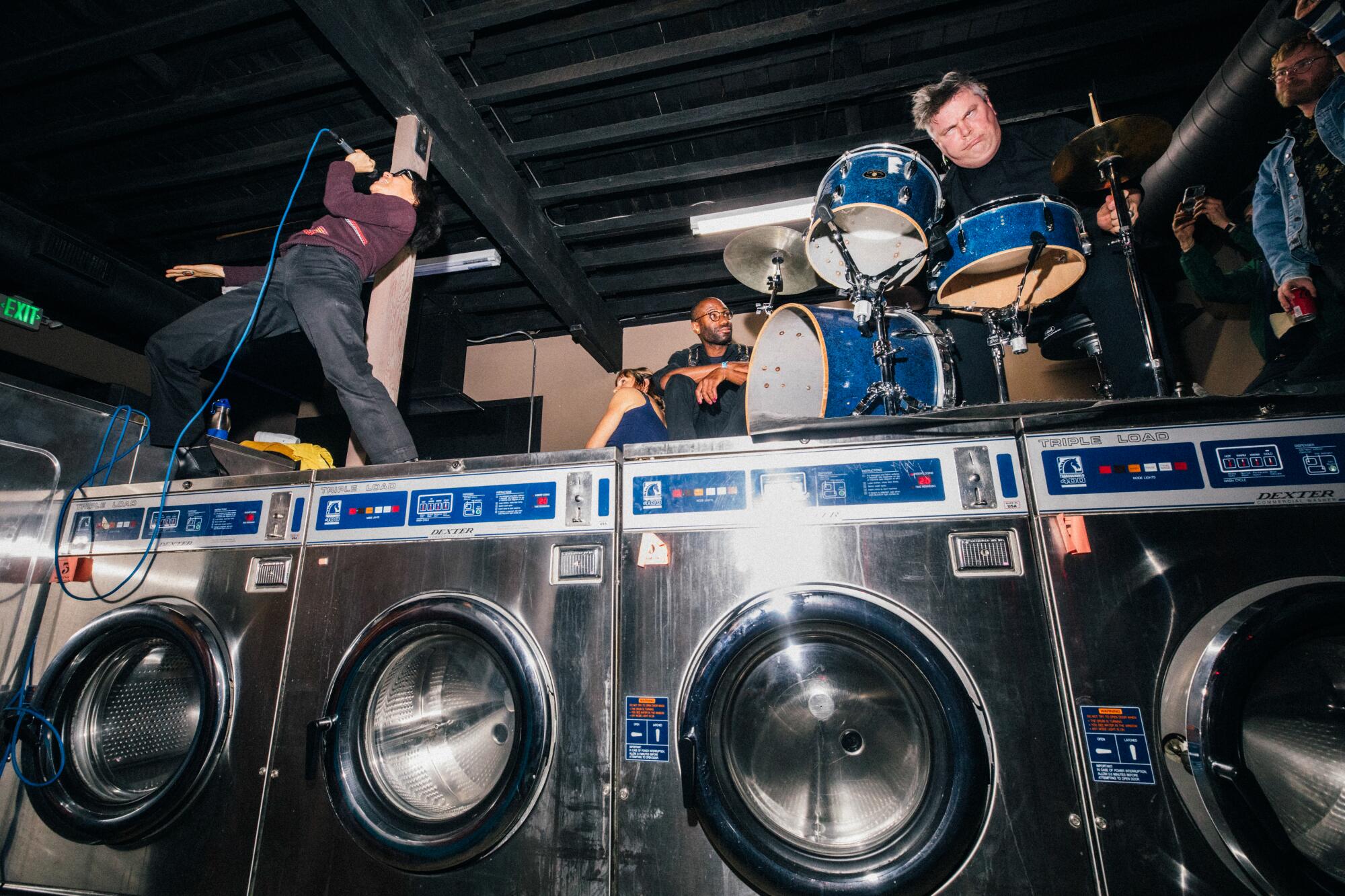 Musicians perform on top of a row of washing machines in a laundromat.