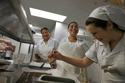 Sara Leong, left, a former methamphetamine addict and mother of four recently released from prison after a grand theft auto conviction, and Felicia Cuellar, center, a mother of three recently released from prison on an assault charge, have a laugh while complimenting Emily Noel as she works on a chocolate cake at the Village Kitchen. The cafe, a project of The Good Shepherd Center for Homeless Women and Children, employs former addicts, dealers, thieves and women who have been down on their luck.