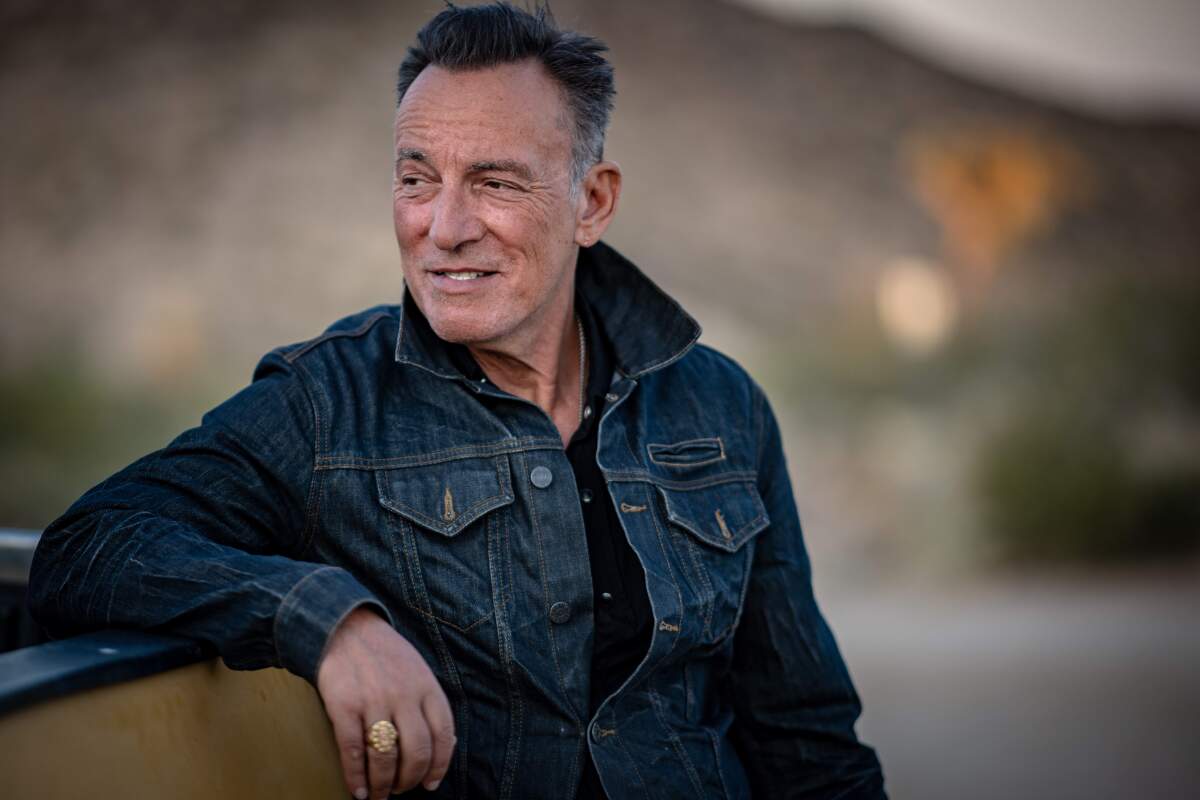 Bruce Springsteen stands in the outdoors in a denim jacket.