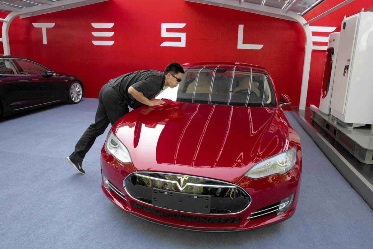 A worker cleans a Tesla Model S sedan before an event to deliver the first set of electric cars to customers in Beijing. The manufacturer has announced plans to boost production.