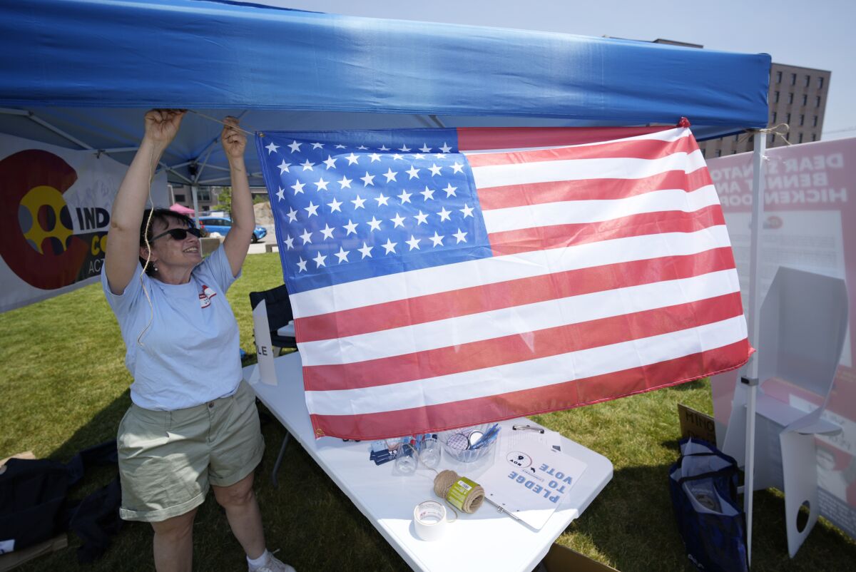 Jody Rein of Centennial, Colo., hangs a United States flag on her group's tent during a rally organized by progressive groups to showcase the state's voting rights Sunday, July 11, 2021, on the campus of Metropolitan State College in downtown Denver. The rally was staged to remind the country what brought the Major League Baseball All Star Game, which will be played Tuesday in nearby Coors Field, from Atlanta to Denver in the first place—that Colorado's elections are among the most accessible and safe in the nation. (AP Photo/David Zalubowski)